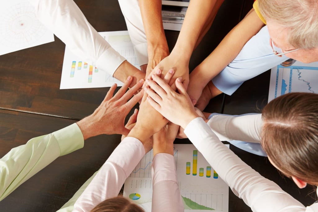 Marketing Strategies for Therapists. Team members stacking hands over a table with graphs and charts to show unity and collaboration.
